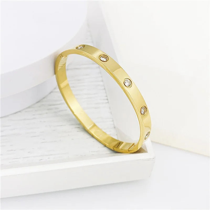 Pulsera y brazalete contemporáneo de cruz con clavo tipo tuerca en zirconia dorada 2023 para mujer en acero inoxidable.