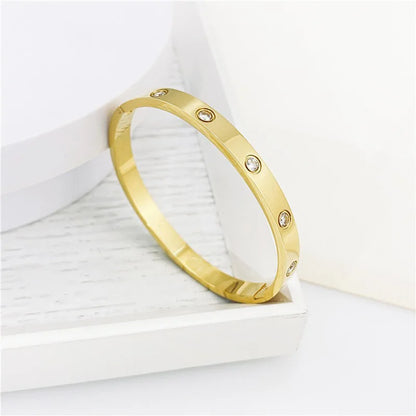Pulsera y brazalete contemporáneo de cruz con clavo tipo tuerca en zirconia dorada 2023 para mujer en acero inoxidable.
