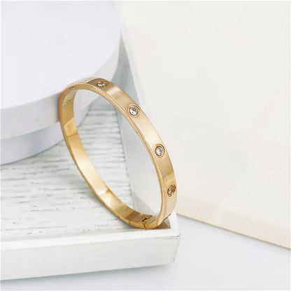 Pulsera y brazalete contemporáneo de cruz con clavo tipo tuerca en zirconia dorada 2023 para mujer en acero inoxidable.